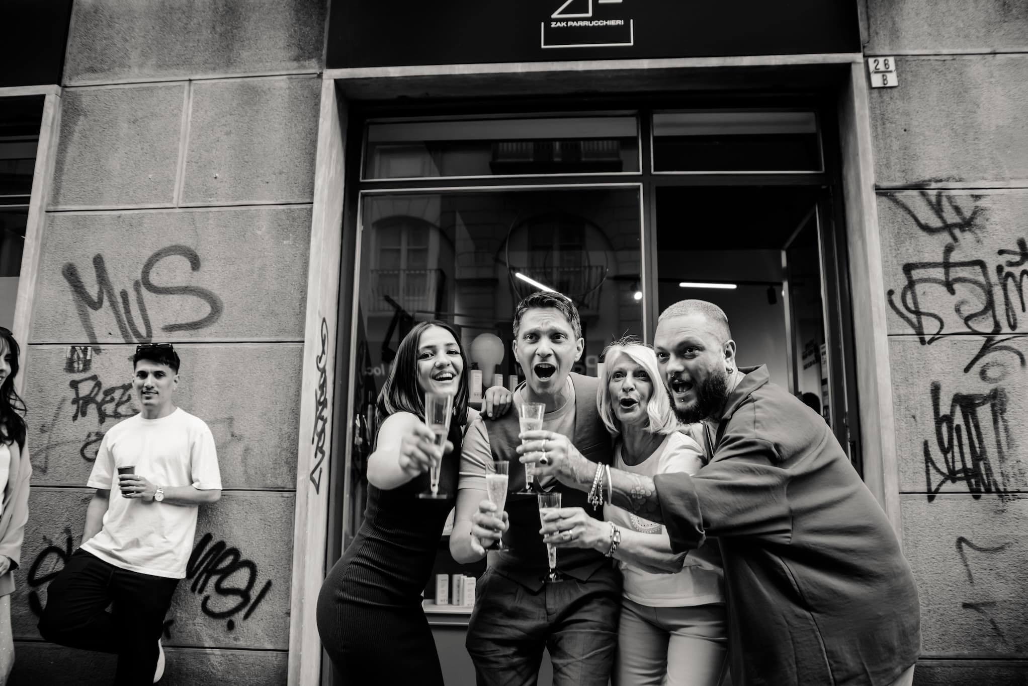 Il proprietario e i suoi collaboratori persone che brindano verso la fotocamera, davanti il negozio di parrucchieri Zak